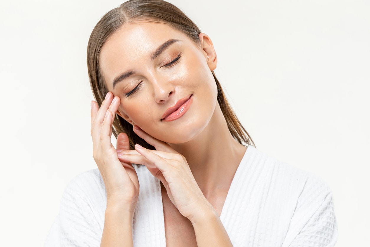 A Woman Closing Her Eyes Feeling Relaxed With Hands Touching Her Face On Isolated White Studio Background.
