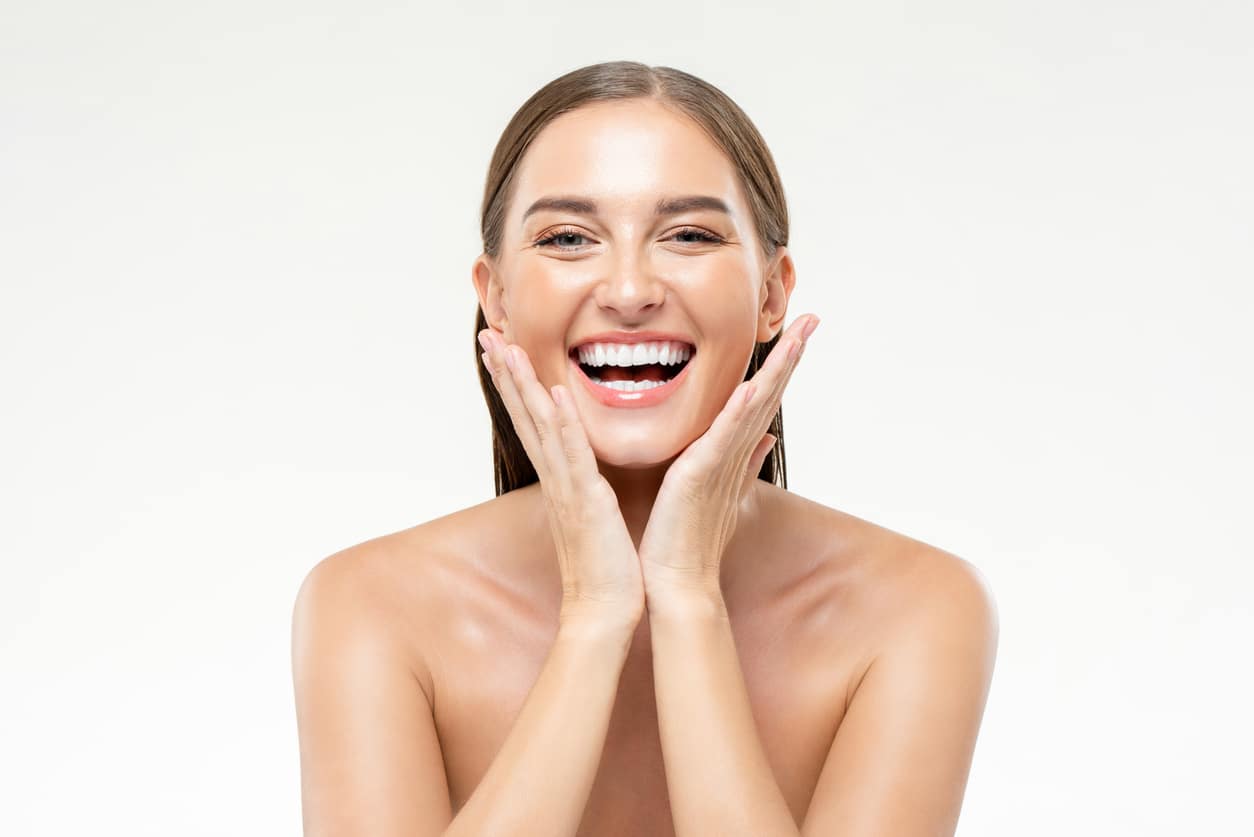 A Young, Smiling, Cheerful Woman With Hands Touching Her Face On An Isolated White Studio Background.